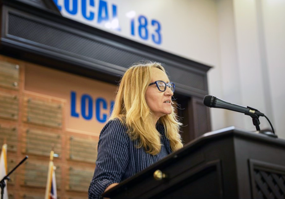 Professor Amanda Grzyb giving a presentation at a podium in a union hall.